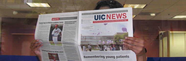 A person reading a UIC News newspaper.